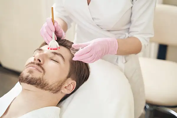 A cosmetologist applying a peeling gel to a man's face